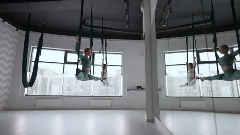 The-interior-shooting-of-an-two-women-practices-different-inversion-antigravity-yoga-with-a-hammock-in-yoga-studio.-The-balance-between-mental-and-physical-two-person-effort-and-achievement-concept